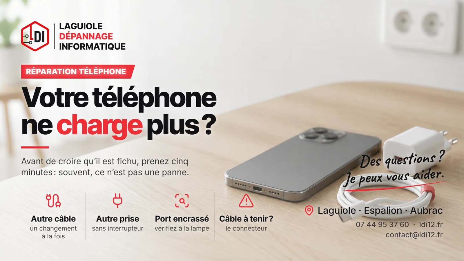 Smartphone posé sur un tapis gris d’atelier, port de charge visible, à côté d’un câble blanc et d’un cure-dent en bois